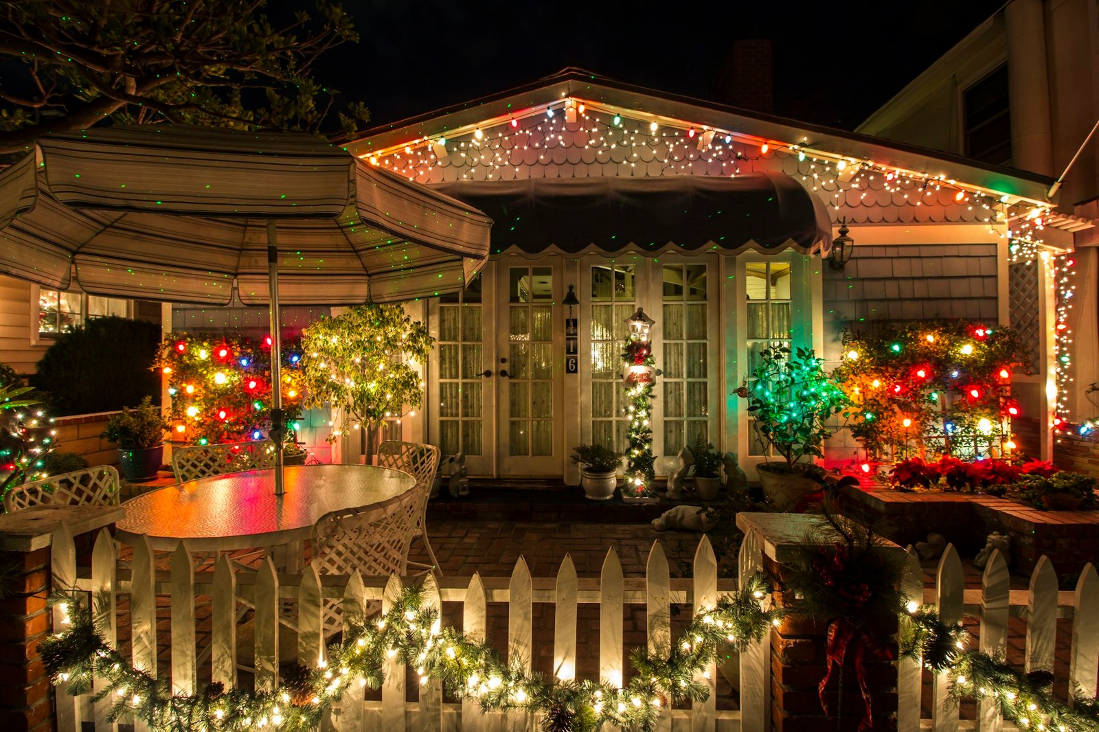 A house decorated with warm custom Christmas string lights along the roofline and lit bushes