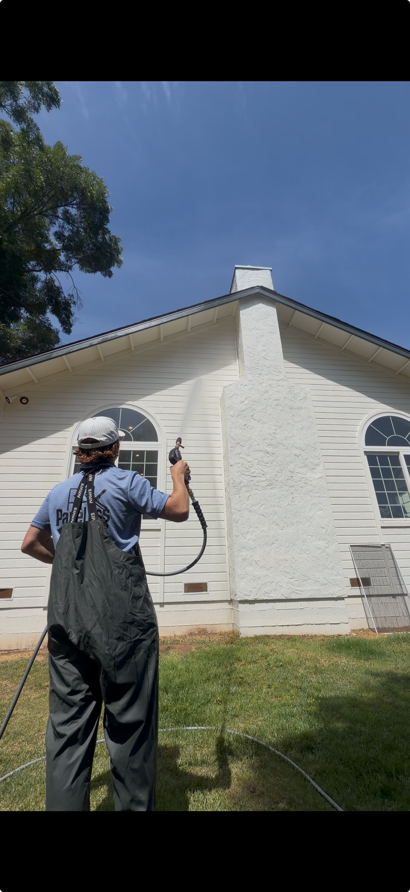 Paneless crew member soft washing a home's siding and chimney